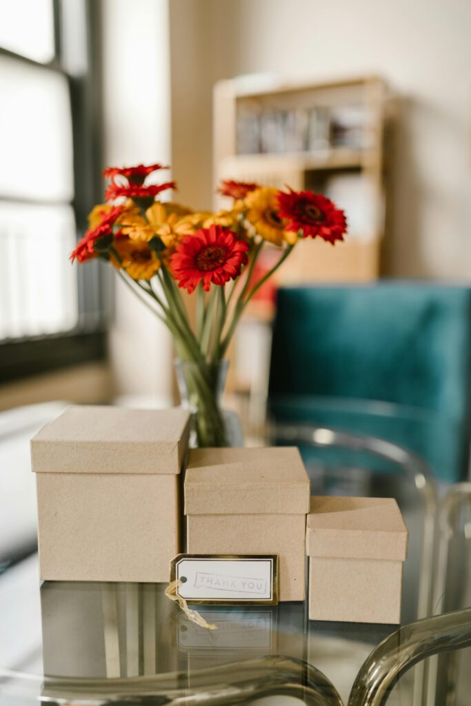 A trio of kraft gift boxes on a glass table, adorned with vibrant flowers, perfect for elegant packaging.